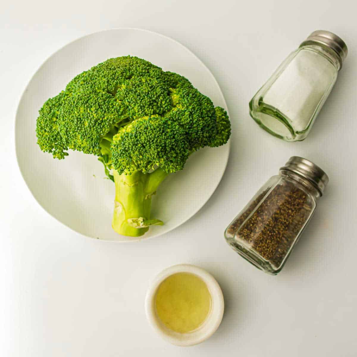 Ingredients to make roasted broccoli on a white surface.