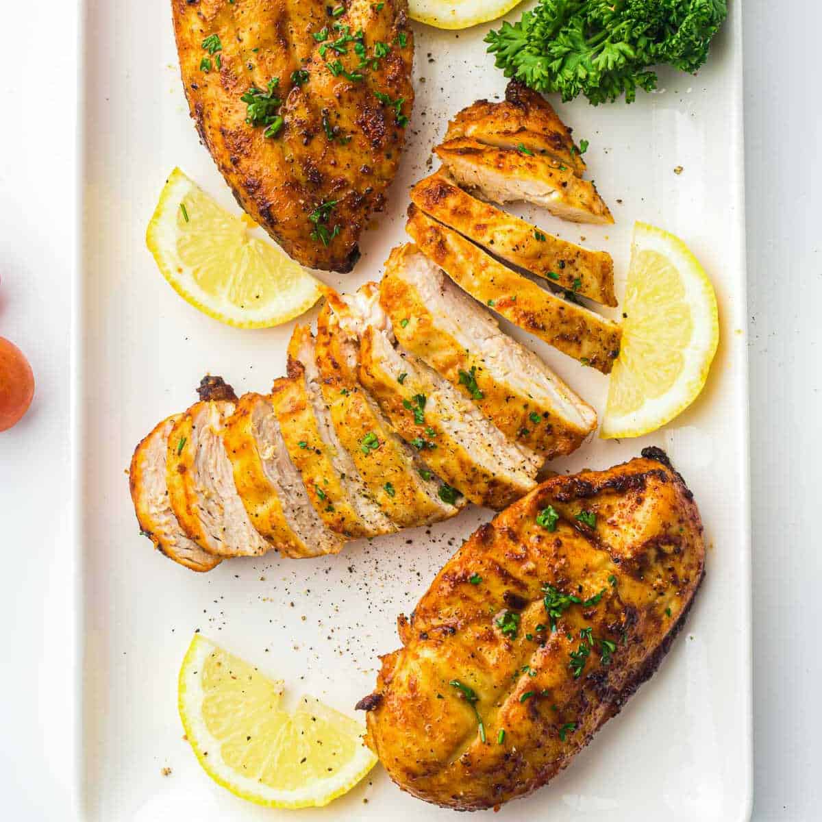 Whole and sliced air fryer chicken breast on a white plate with lemon slices in the background.