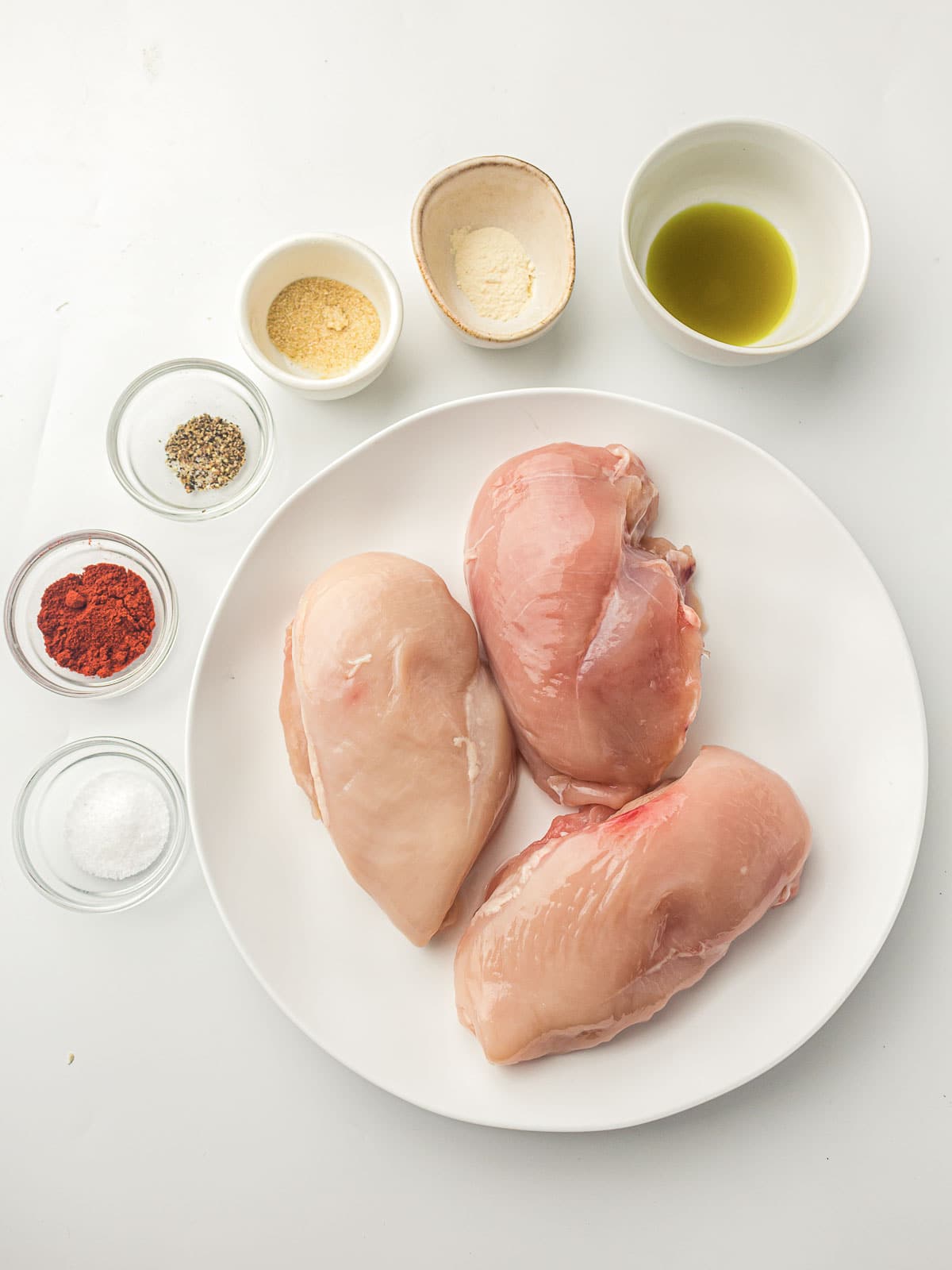 Ingredients to make air fryer chicken breast on a white surface.