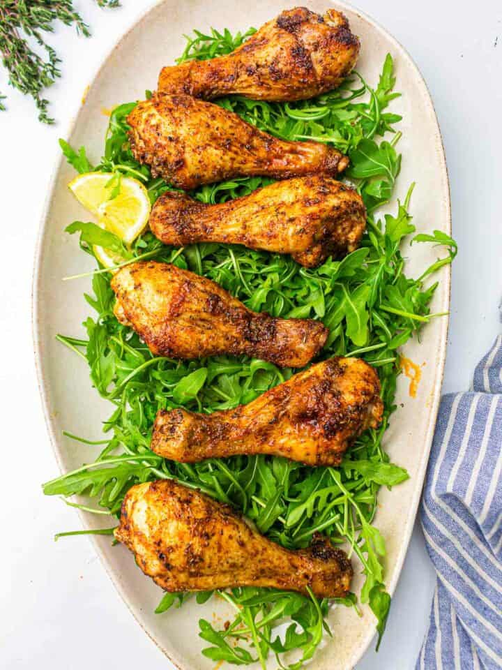 AIr fryer chicken drumsticks on a bed of arugula leaves on white plate.