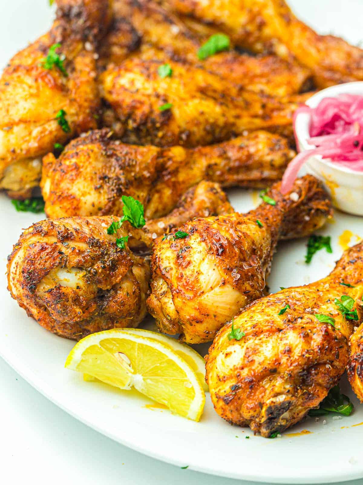 Chicken drumsticks served with lemon wedges and pickled onions.