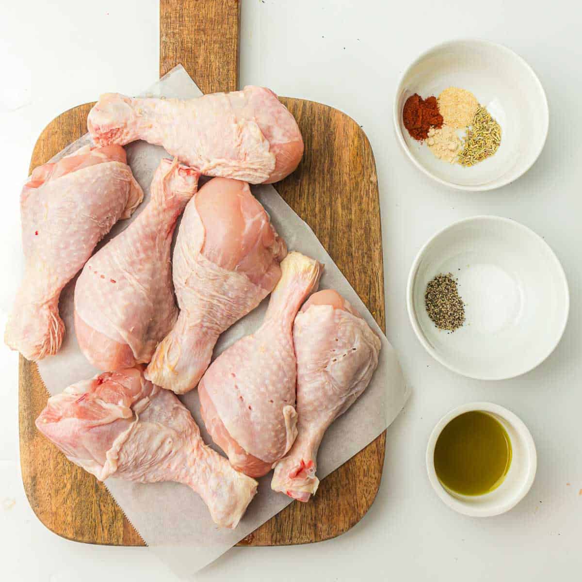 Ingredients to make air fryer chicken drumsticks on a white surface.