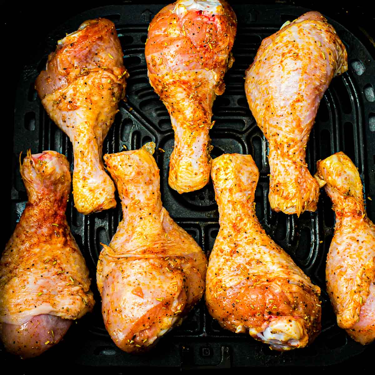 Marinated chicken drumsticks in air fryer basket.