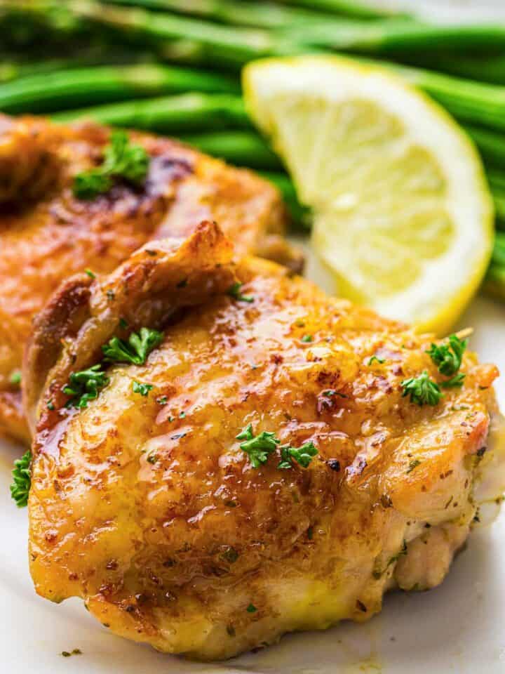 Air fryer chicken thighs served with green beans and lemon wedge on a white plate.