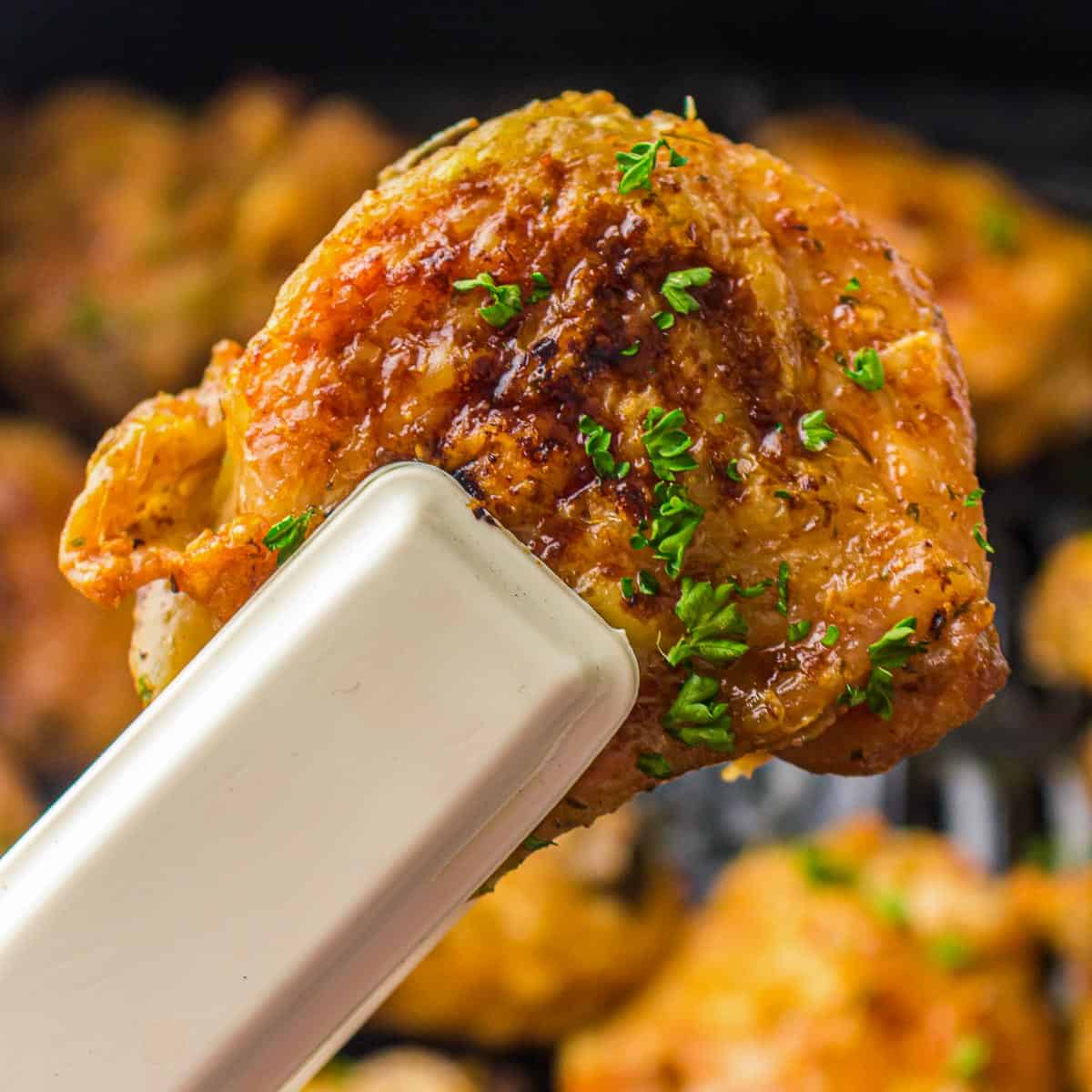 Holding roasted chicken thigh using tongs.