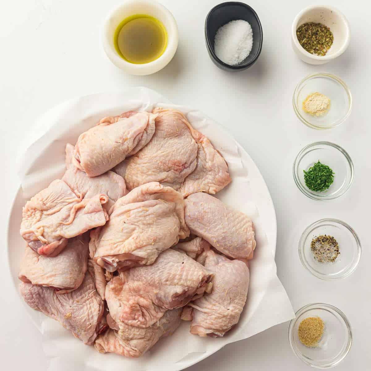 Ingredients to make air fryer chicken thighs on a white surface.