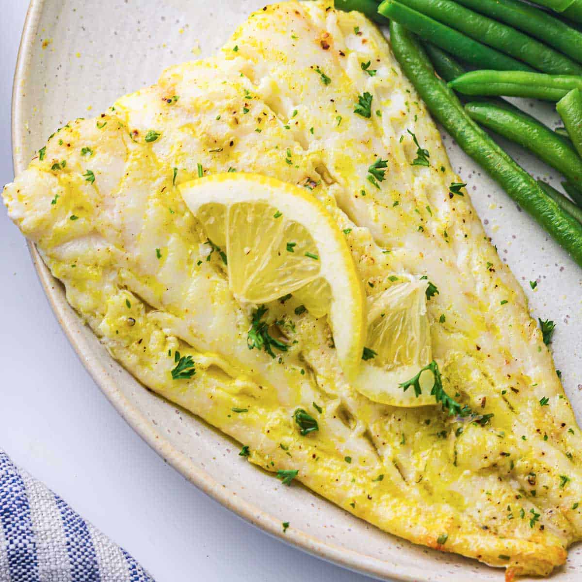 Cod fillet on a white plate garnished with lemon slice.