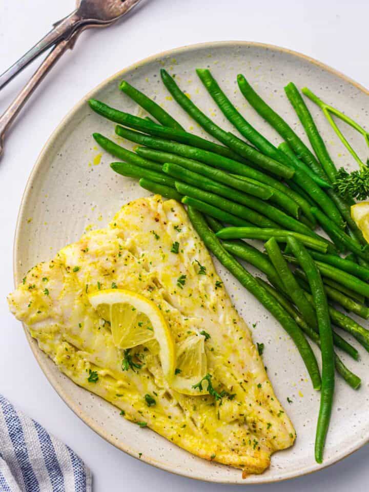 Cod fish served with green beans on a white plate.