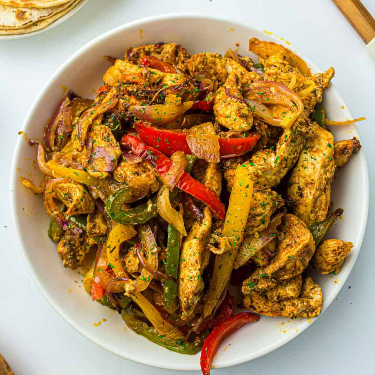 Air fryer chicken fajitas in a white bowl with tortillas in the background.