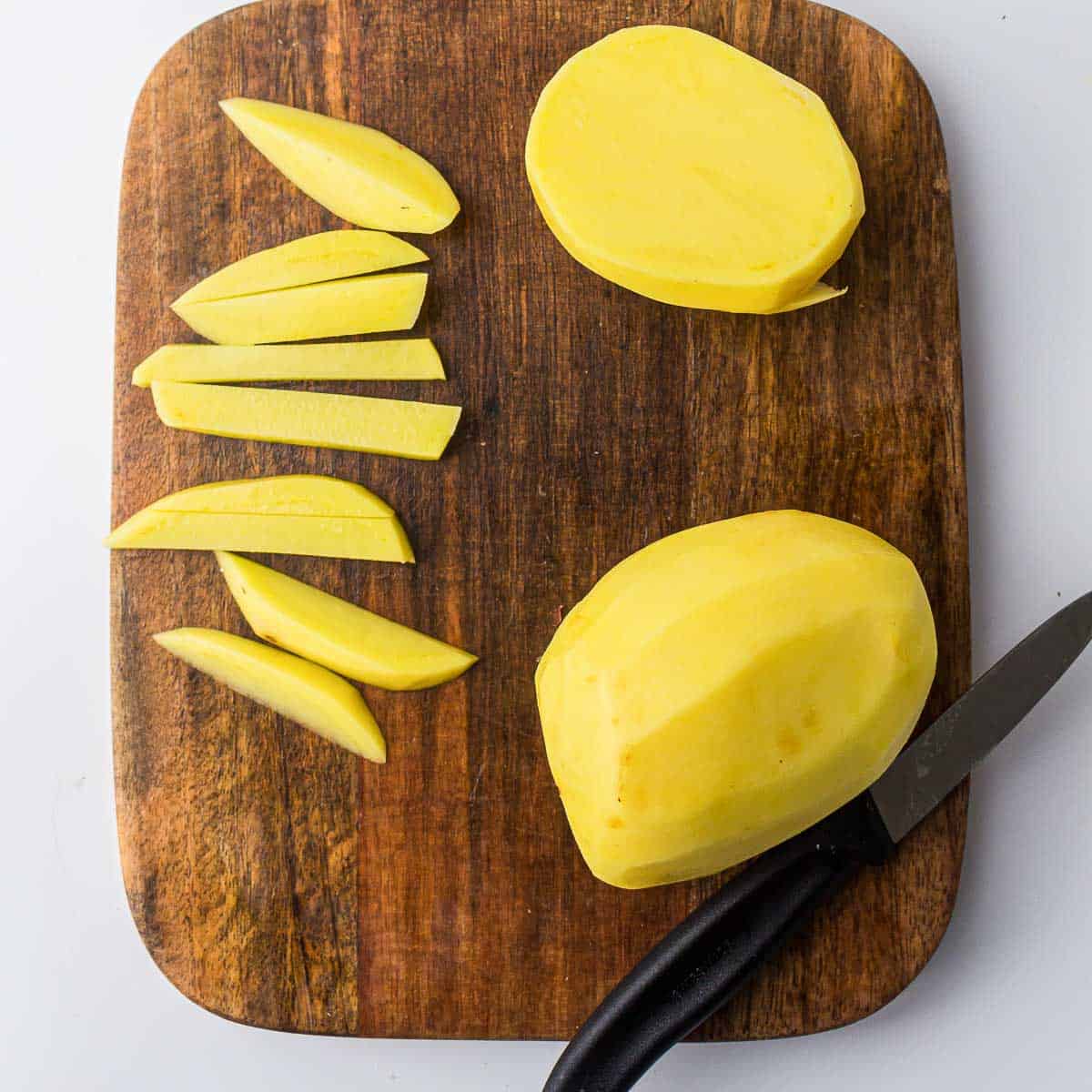 Peeling and cut potatoes on a wooden board.