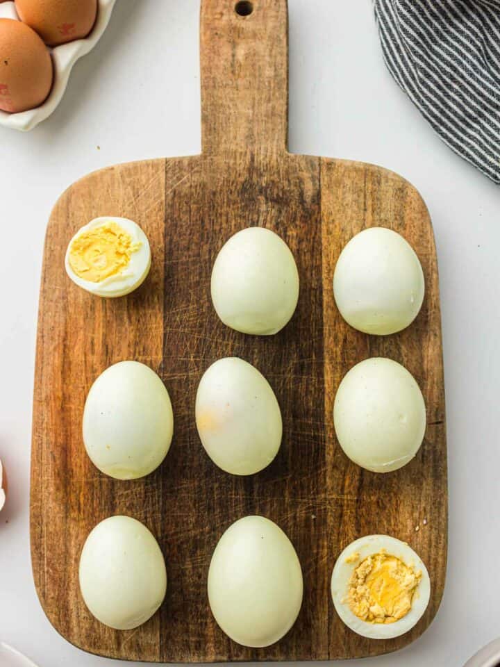 Peeled boiled eggs on a wooden board placed on a white surface.