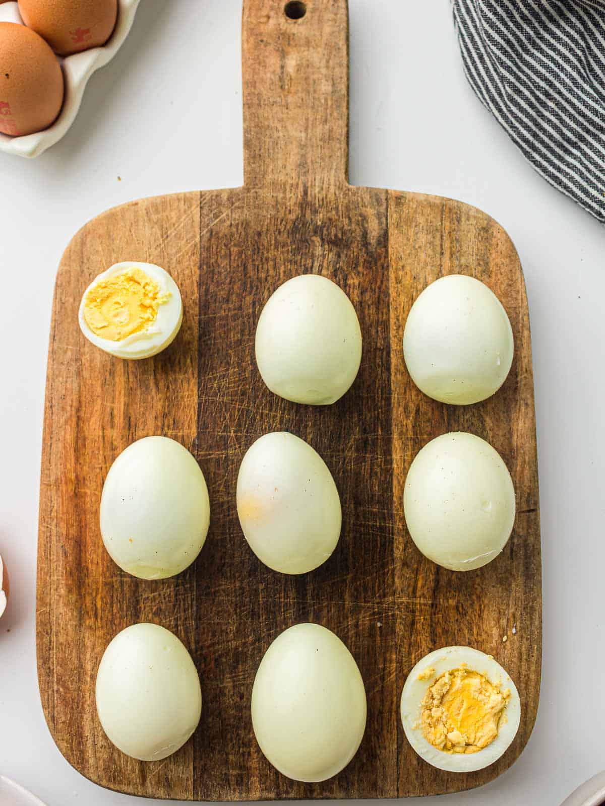 Peeled boiled eggs on a wooden board placed on a white surface.