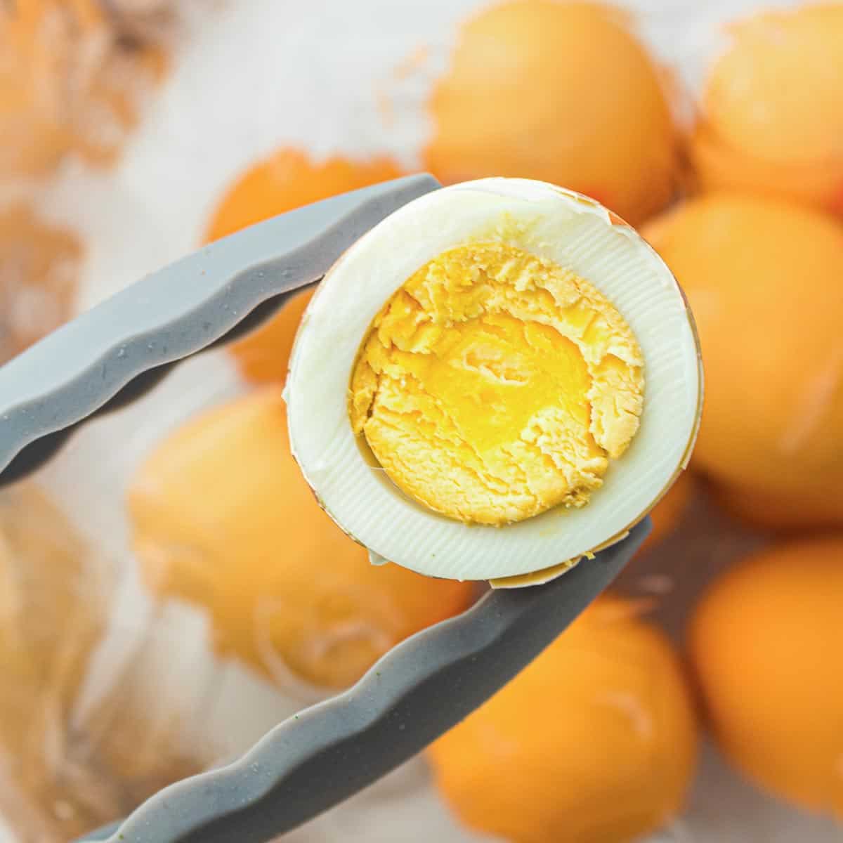 Holding boiled egg using a tong with unpeeled eggs in the background.