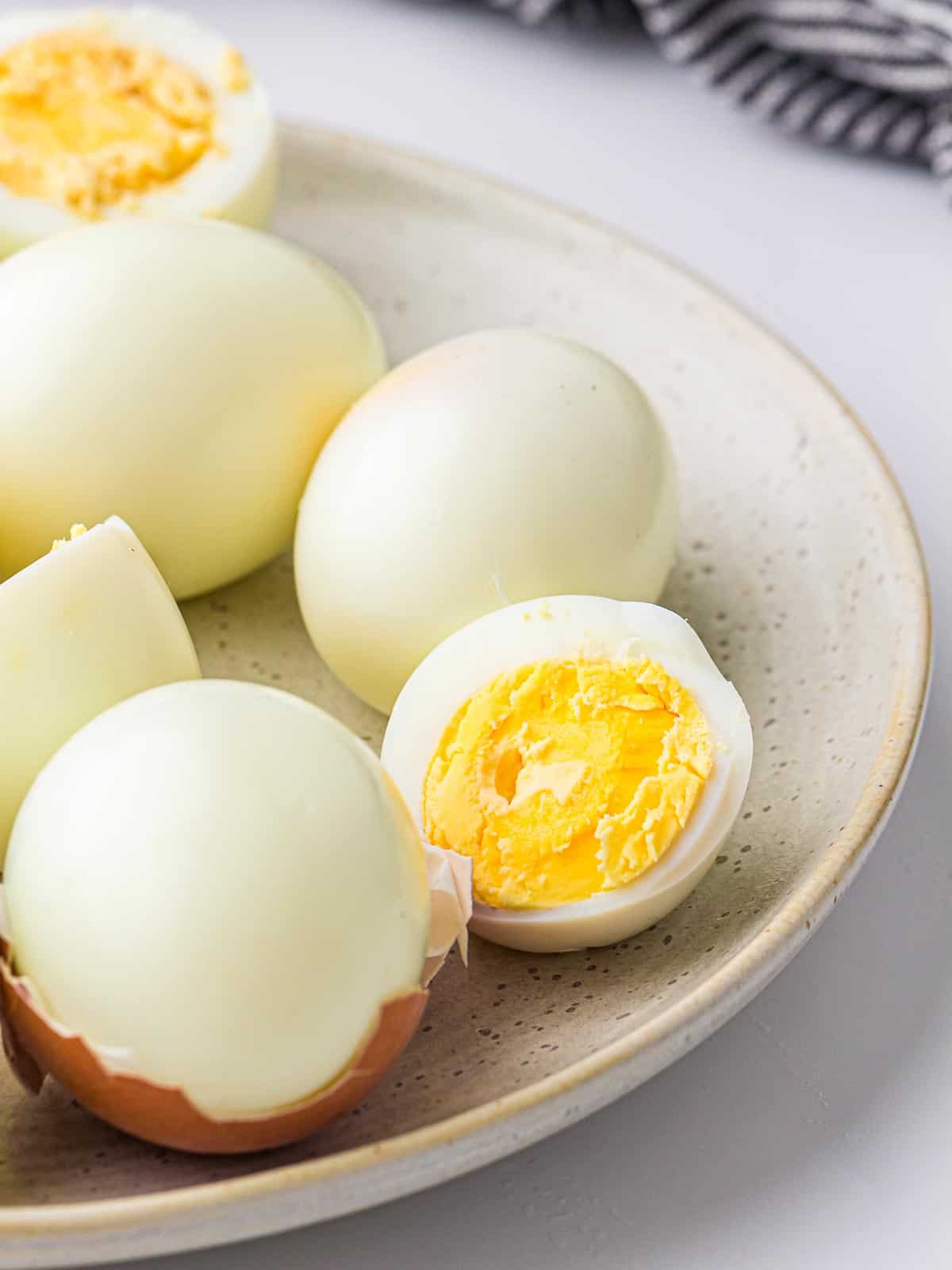 Close up of peeled and unpeeled boiled eggs on a white plate.