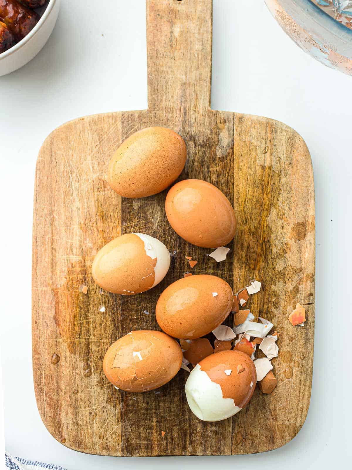 Peeled and unpeeled boiled eggs on a wooden board.