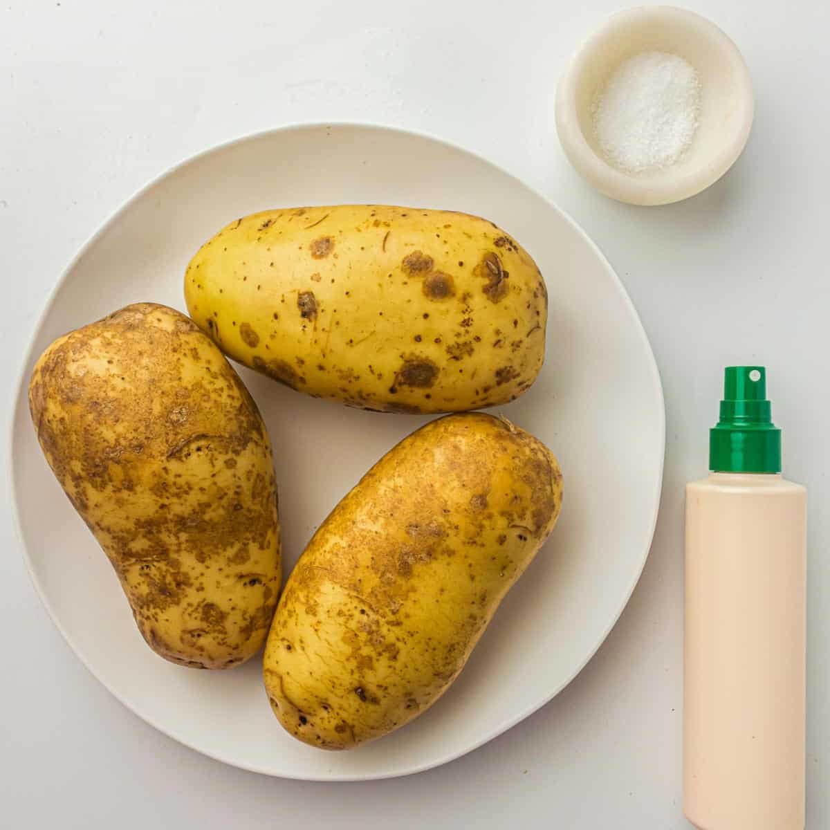 Ingredients to make jacket potatoes on a white surface.