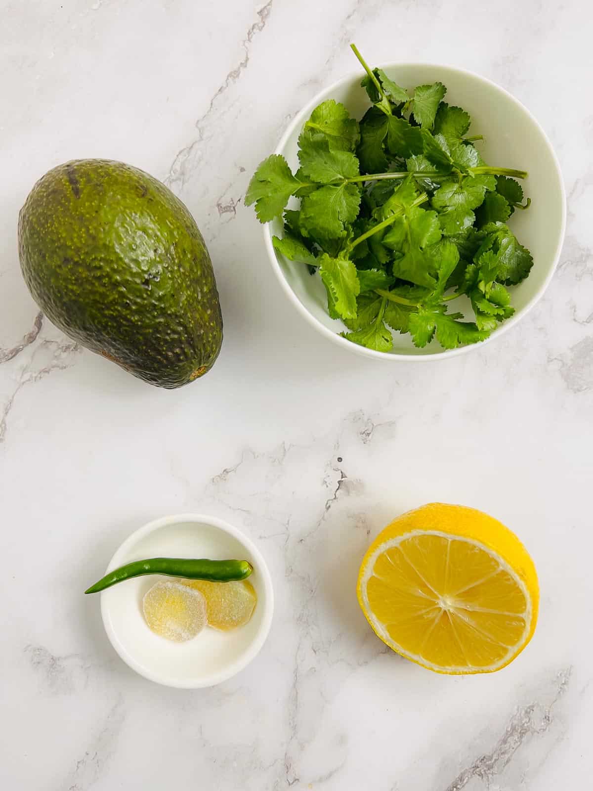 Ingredients to make avocado cilantro chutney on a marble surface.