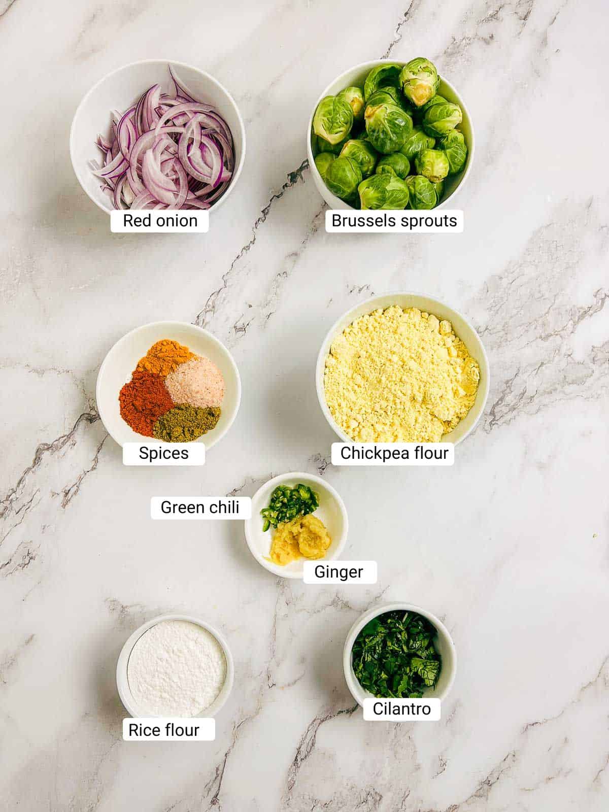 Ingredients to make Brussels sprouts pakora on a marble surface.