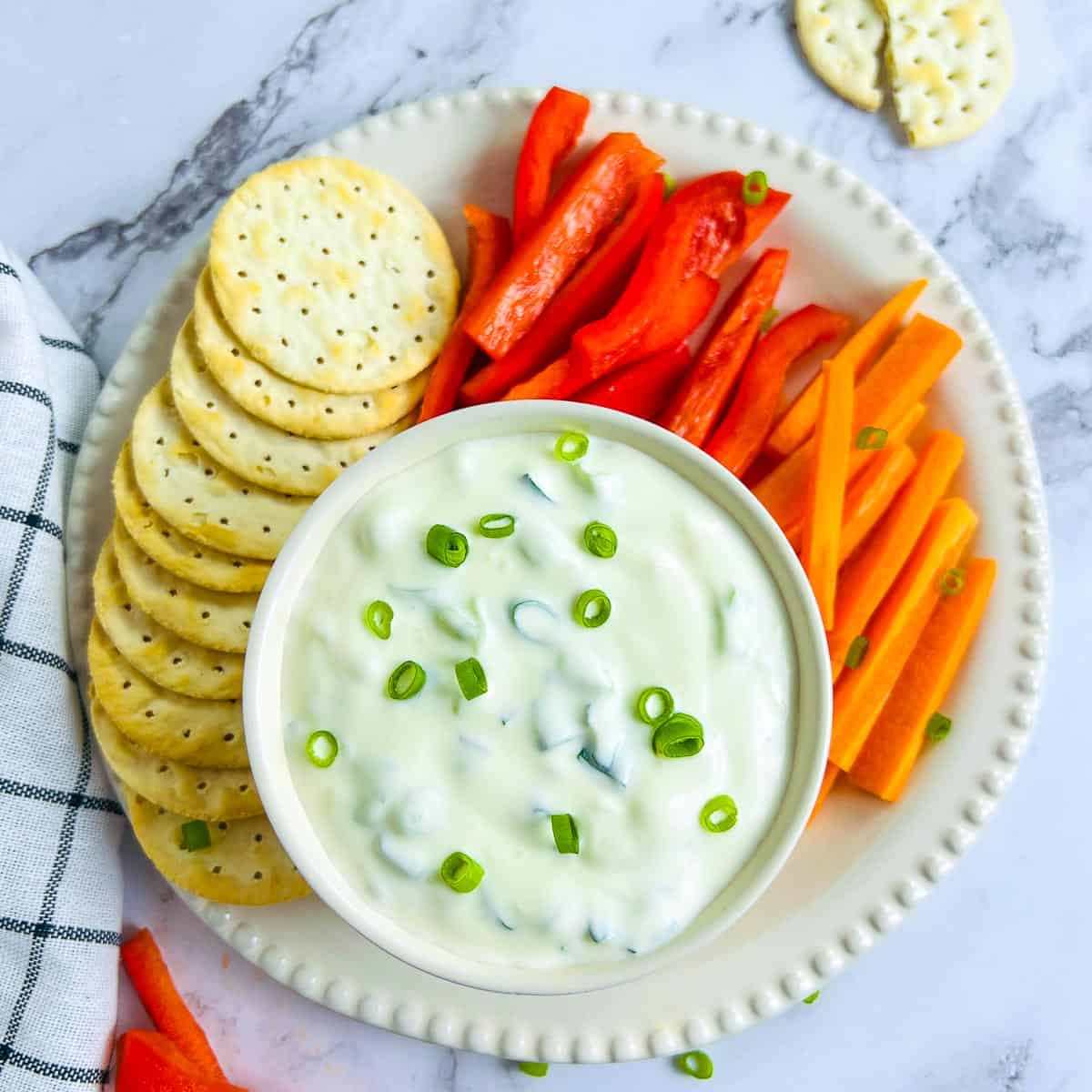 Green onion dip in a bowl with vegetables and crackers in the background.