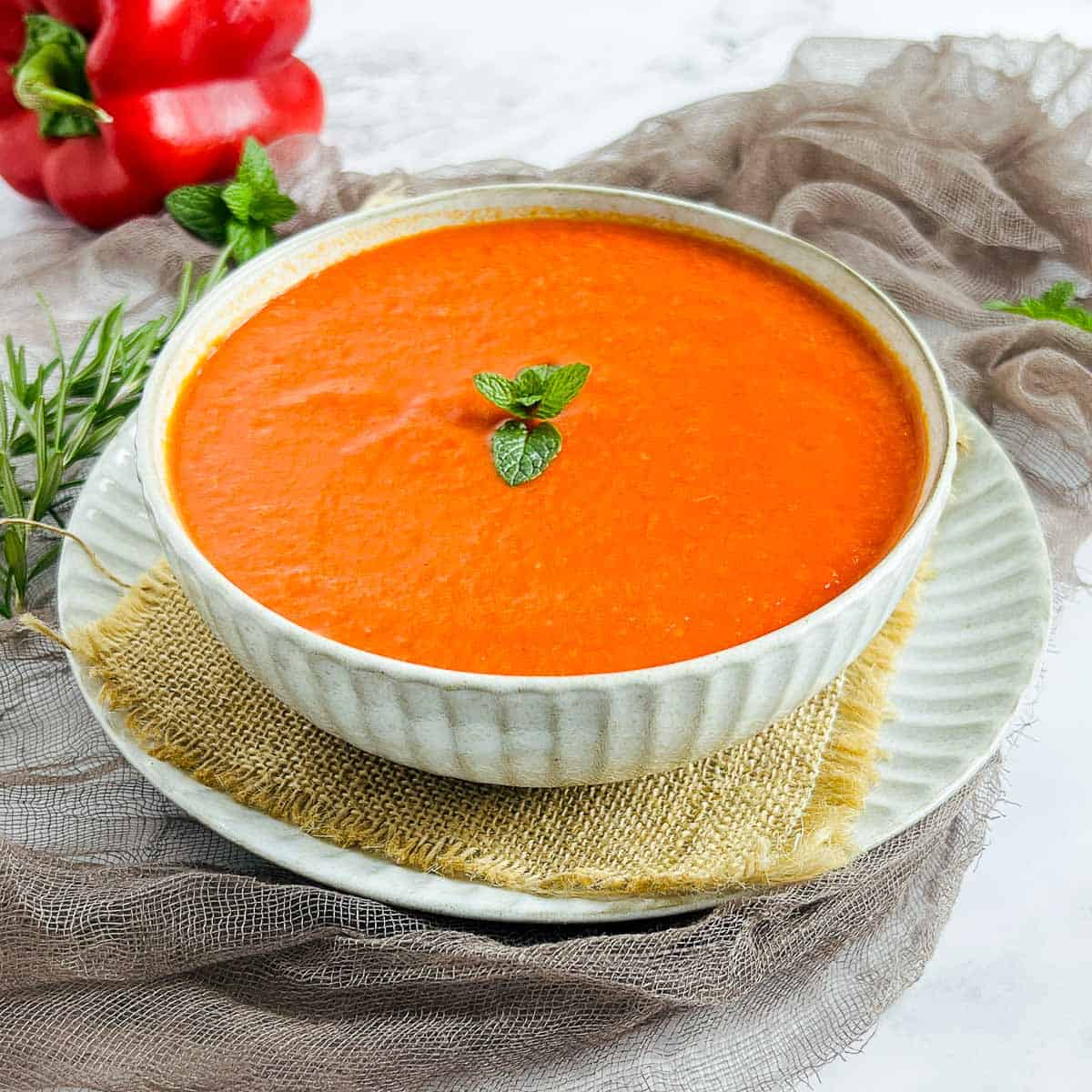 Roasted bell pepper and habanero sauce in a white bowl with bell peppers in the background.