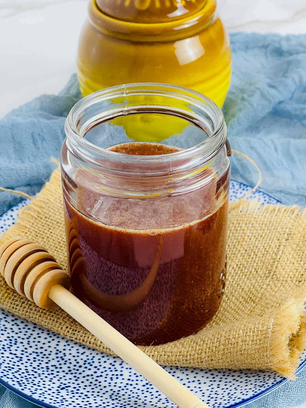 Hot honey in a jar for storing with honey drizzle in the background.