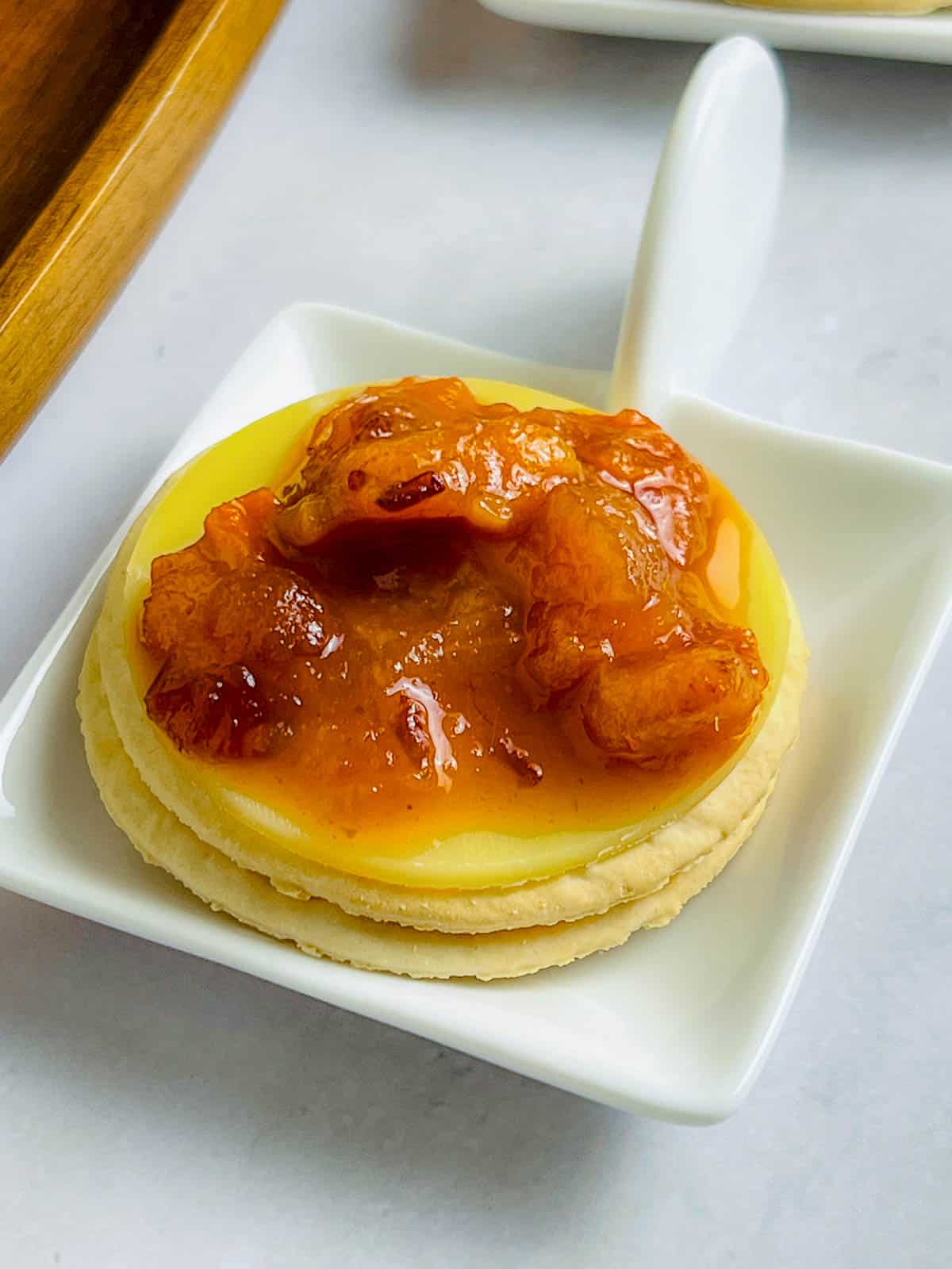 Persimmon chutney topped on a cracker and a slice of cheese.