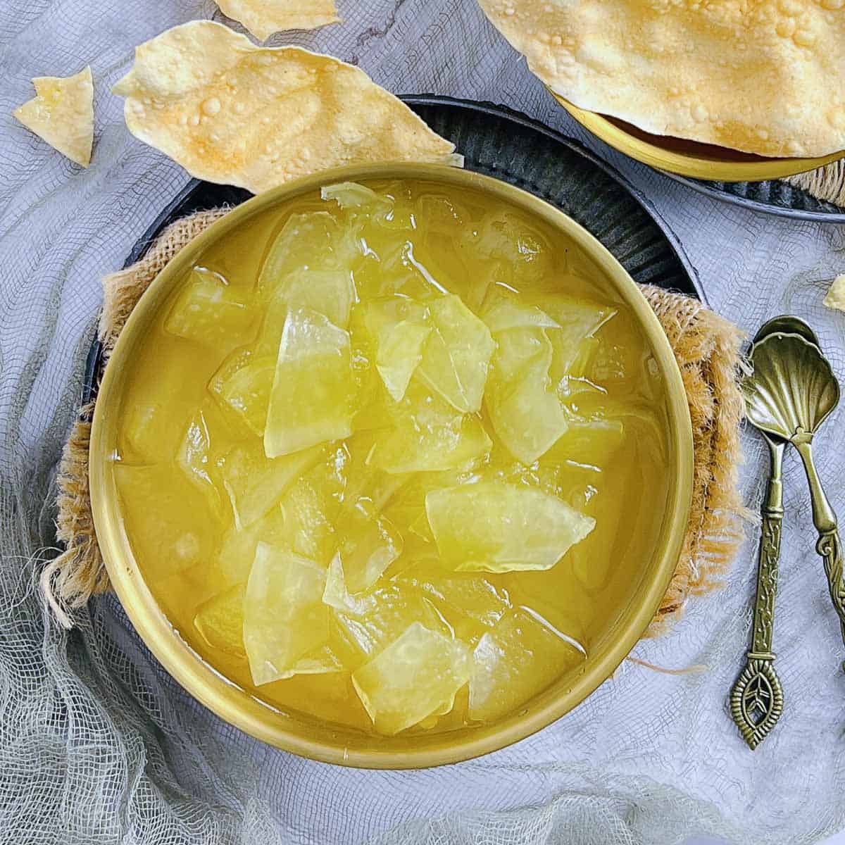 Plastic chutney in a wide bowl with spoons and papad in the background.