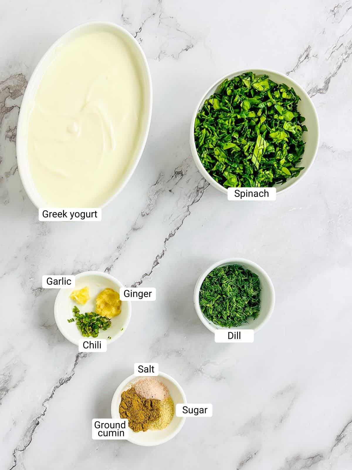 Ingredients to make spinach dill raita on a marble surface.