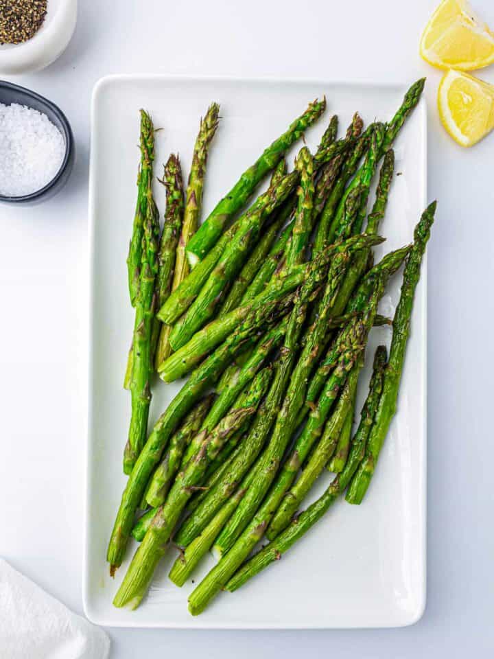 Air fryer asparagus on a rectangular plate served with lemon wedges.