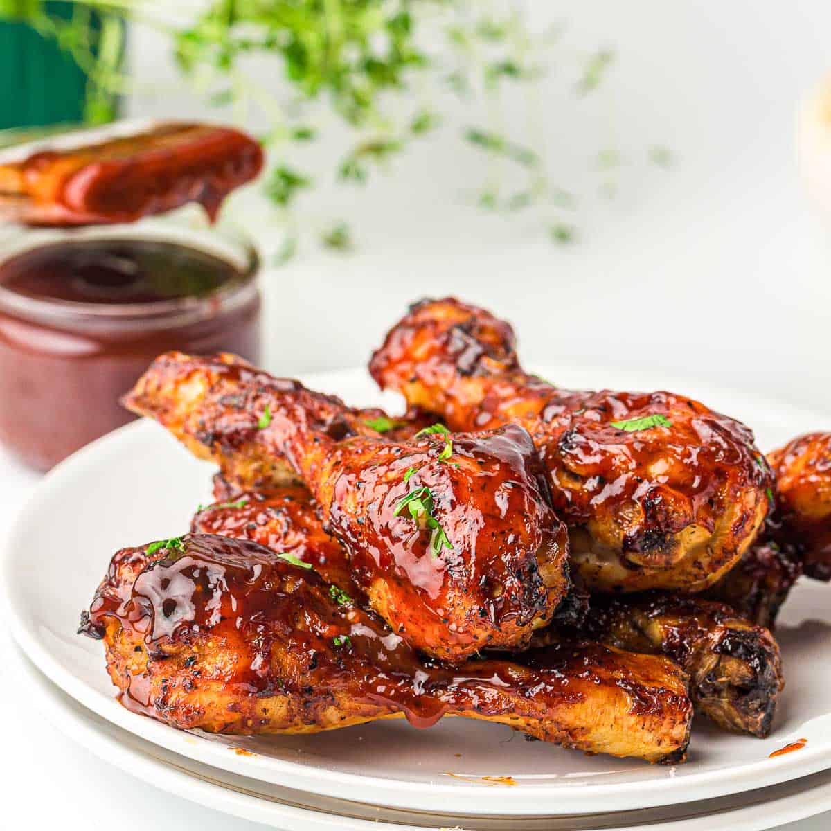 Bbq chicken on a white plate with bbq sauce in the background.