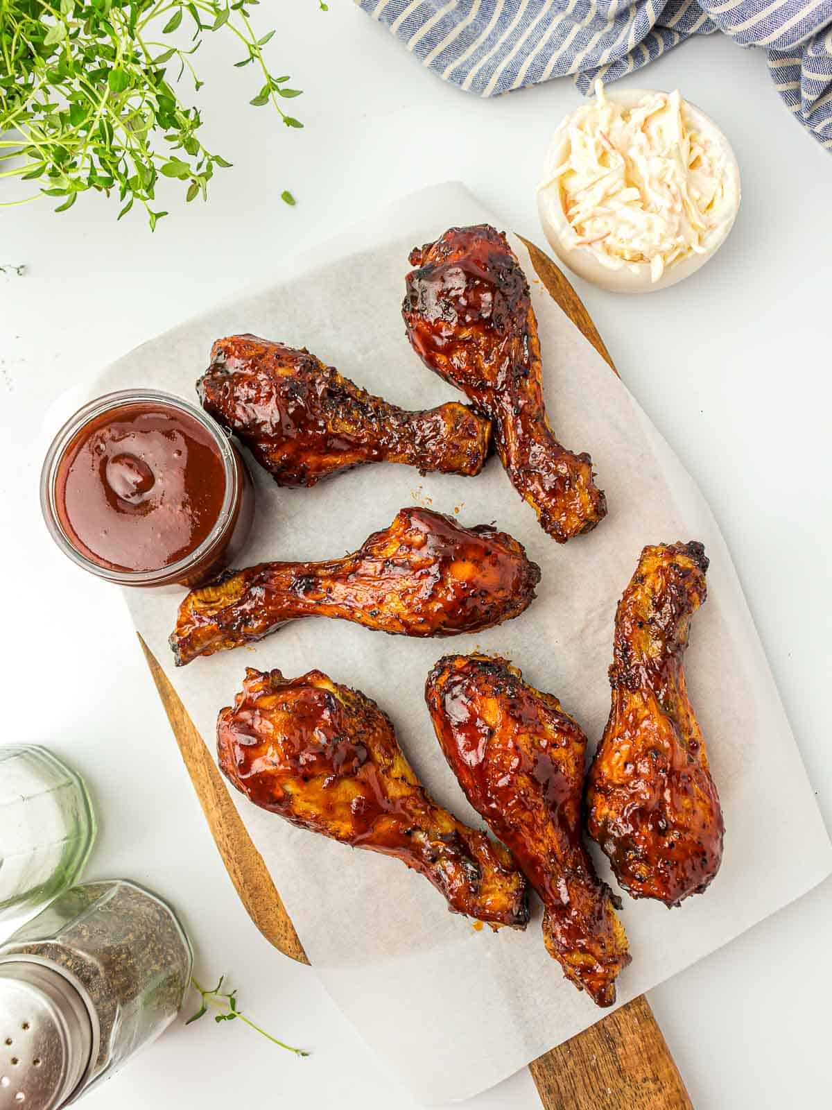 BBq chicken on a wooden board with bbq sauce in the background.