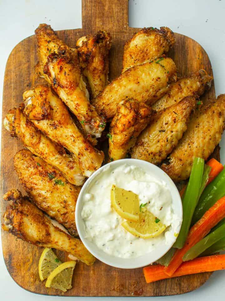 Air fryer chicken wings on a wooden board served with dip.