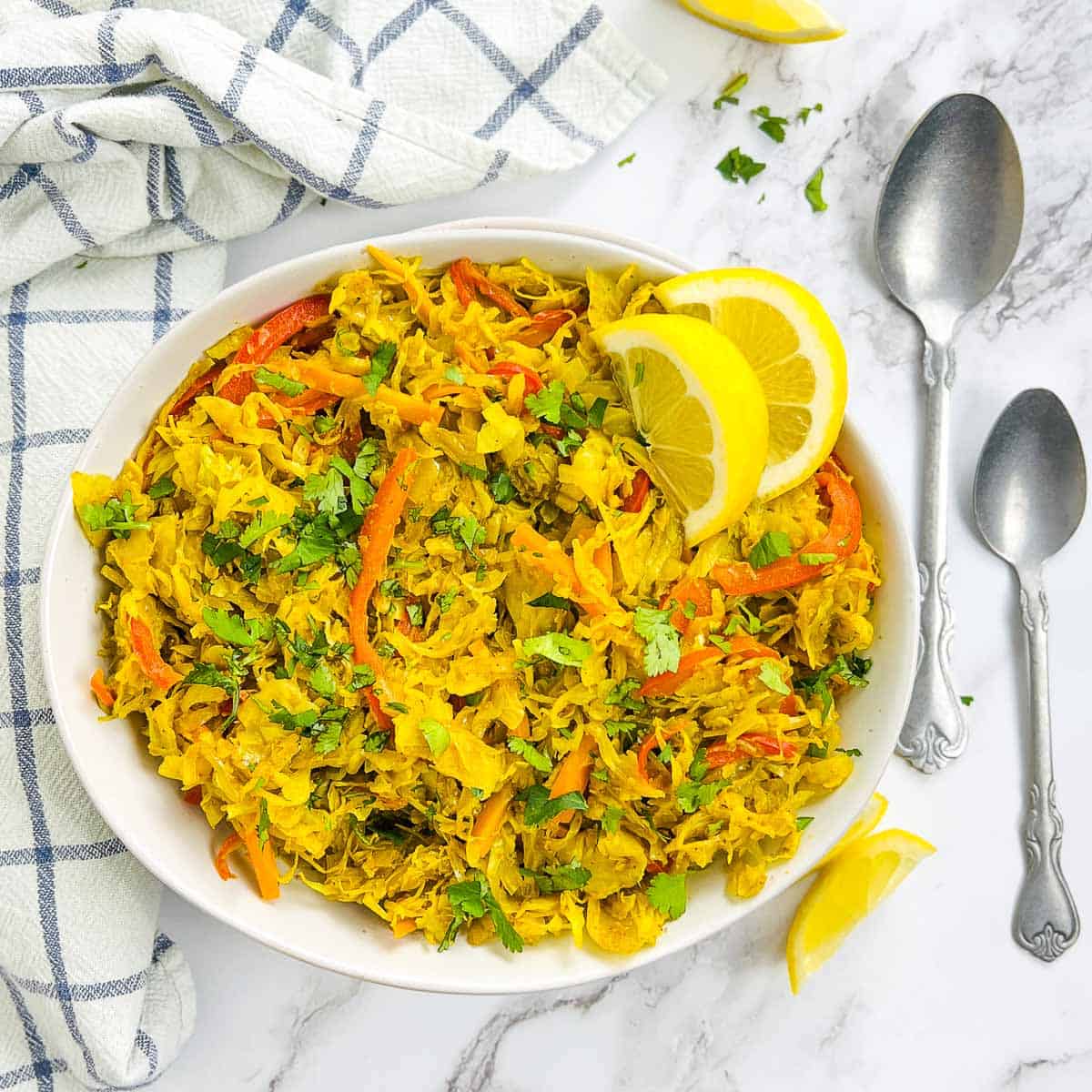 Curried cabbage stir fry in a white bowl garnished with lemon wedges.