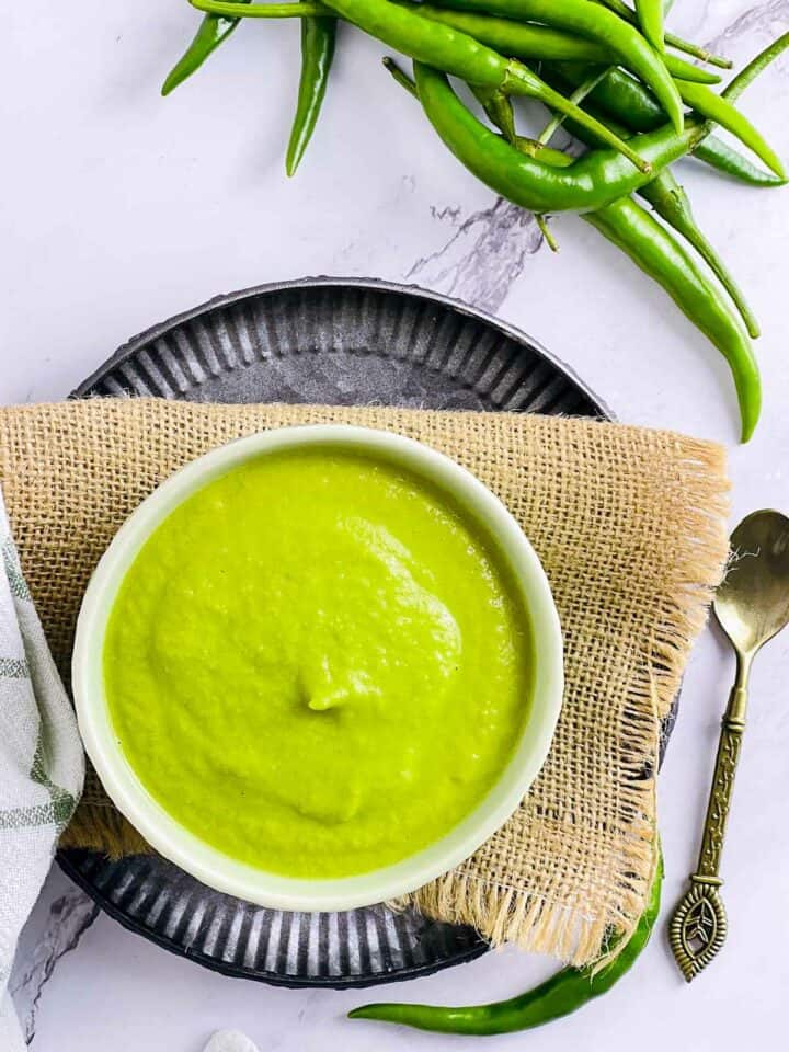 Green chili sauce in a small bowl with chilies in the background.