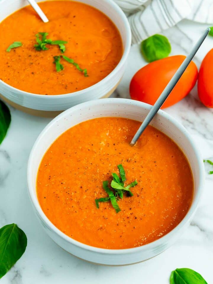 Two bowls of tomato soup on a white surface.