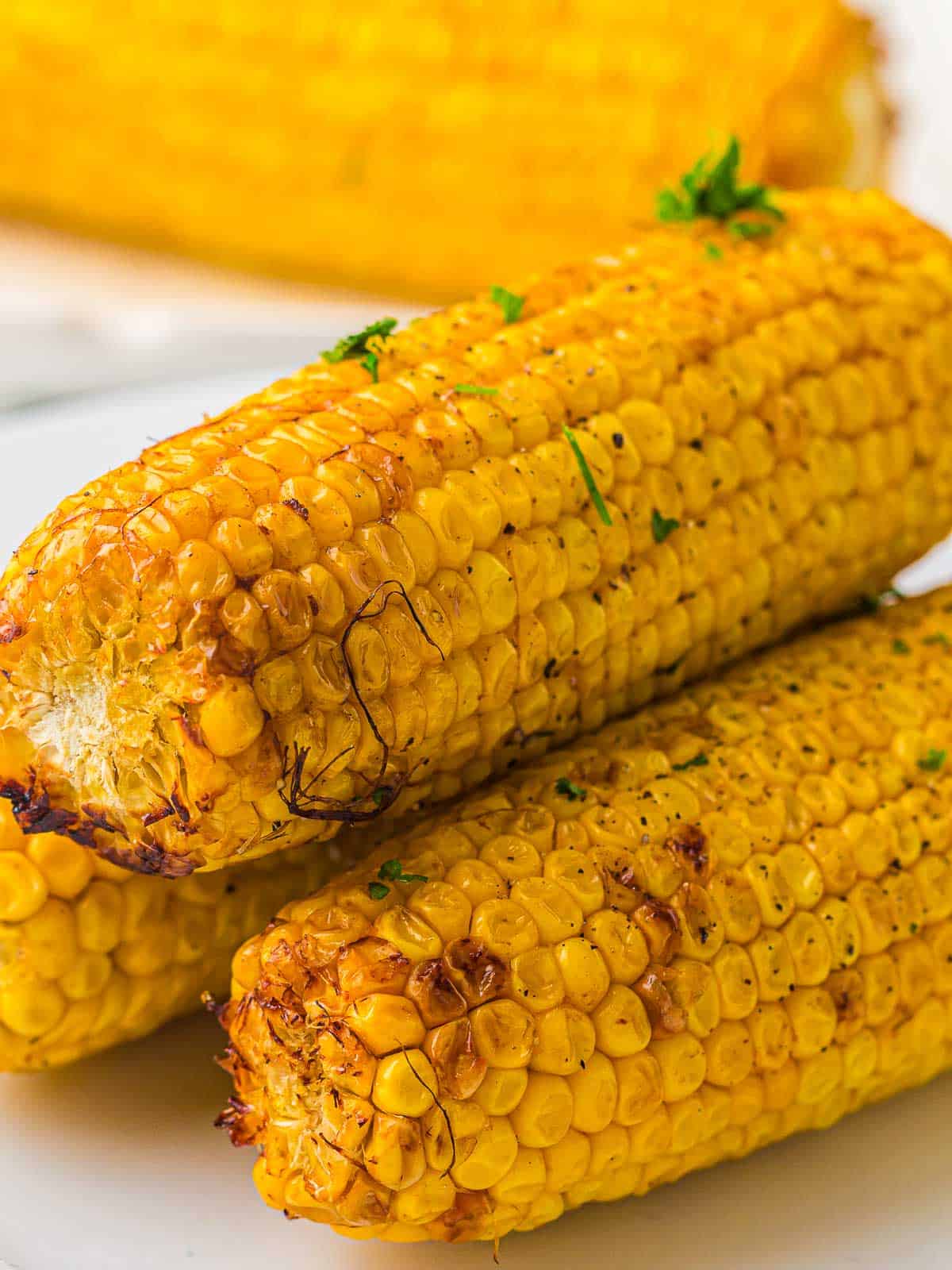 Stack of roasted corn on a white plate.