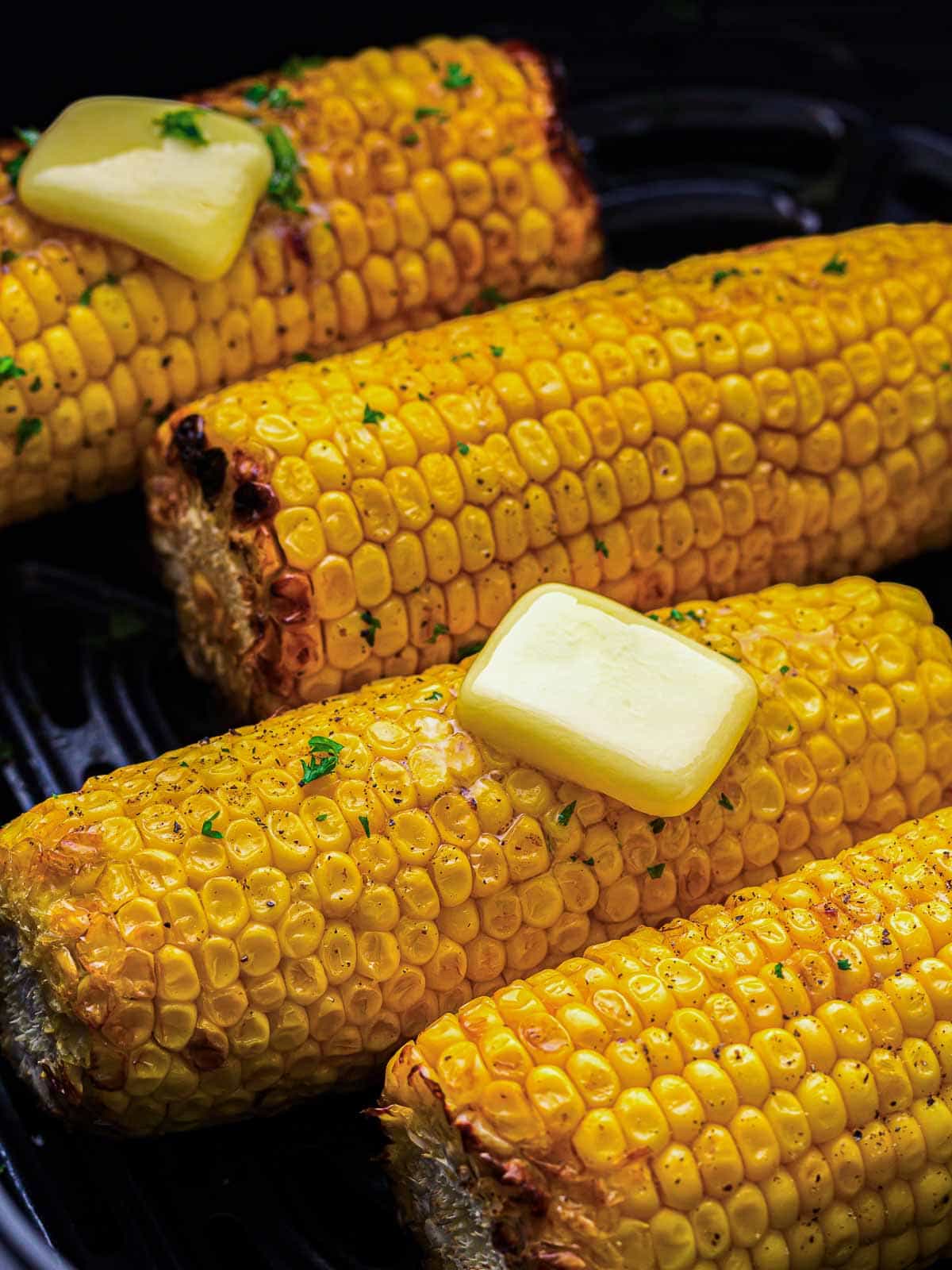 Roasted corn topped with butter in the air fryer basket.