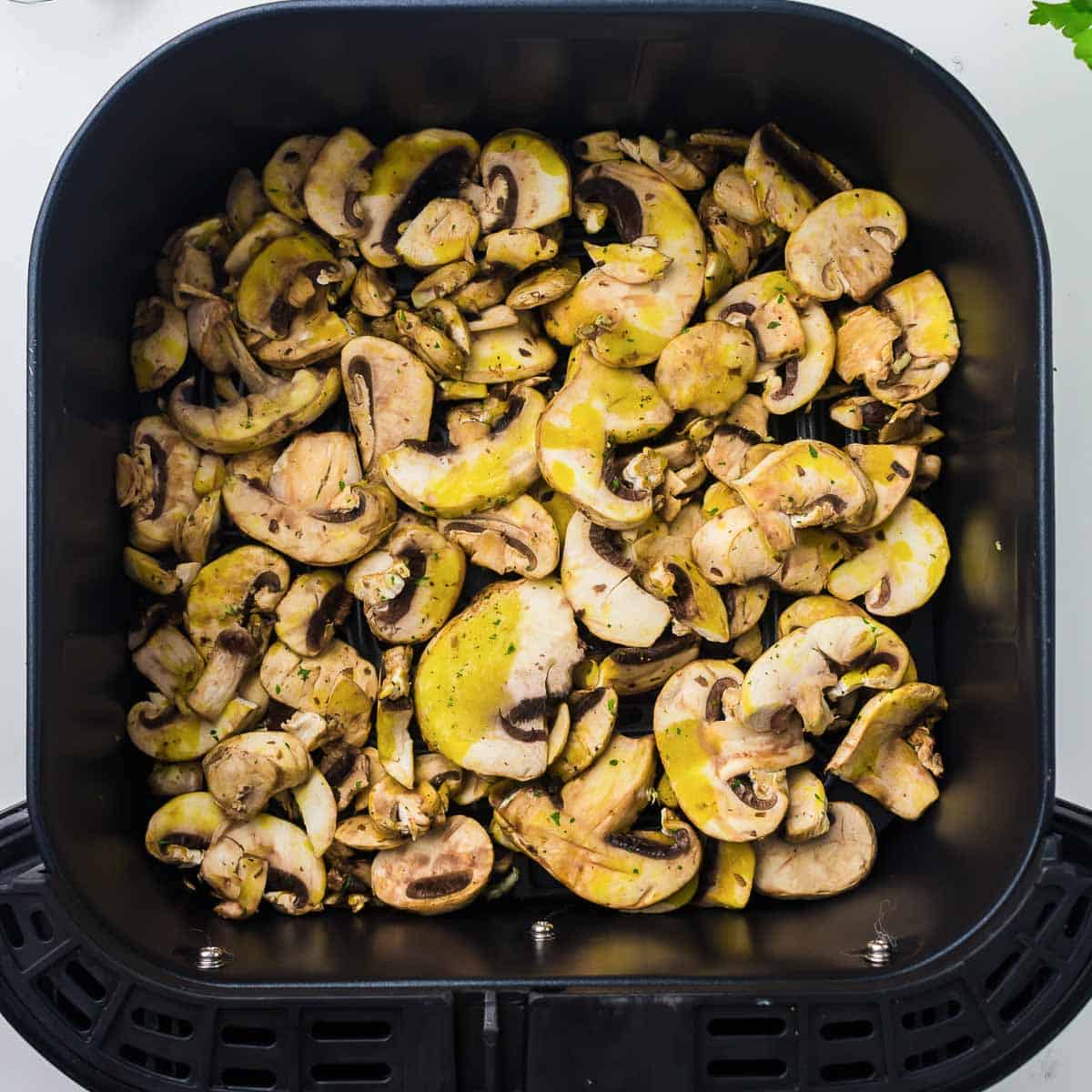 Seasoned mushroom slices spread in the air fryer basket.