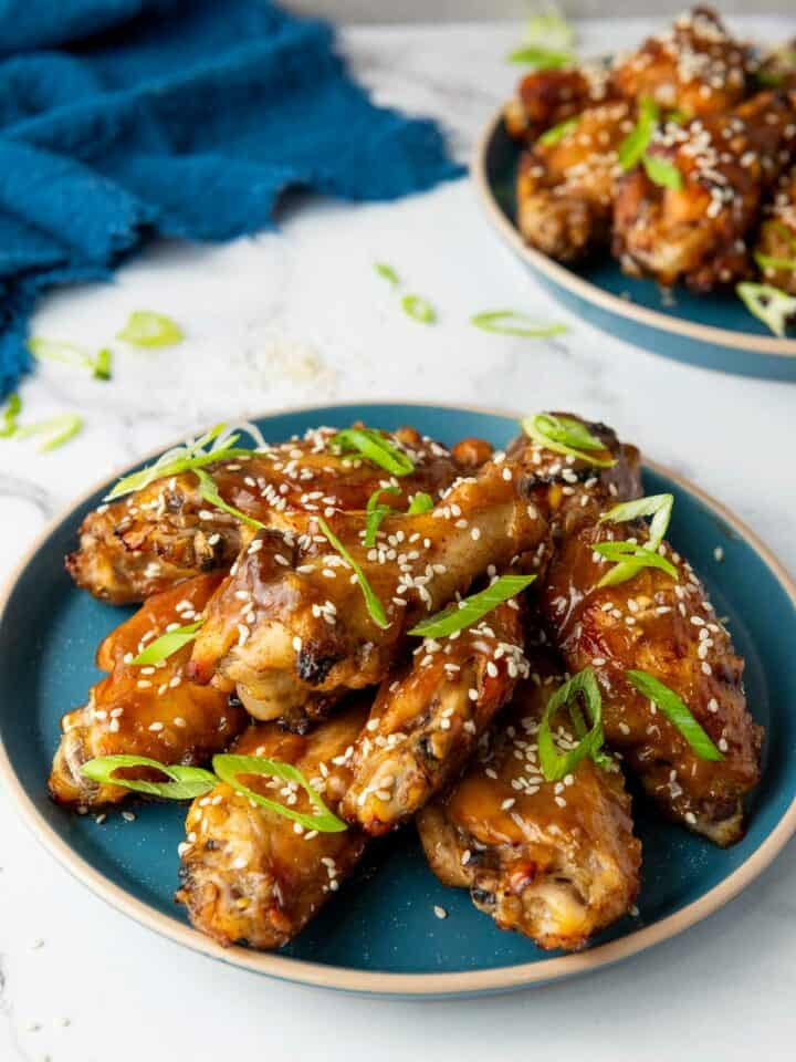 Asian sticky chicken wings on a blue plate garnished with sesame seeds and scallion.