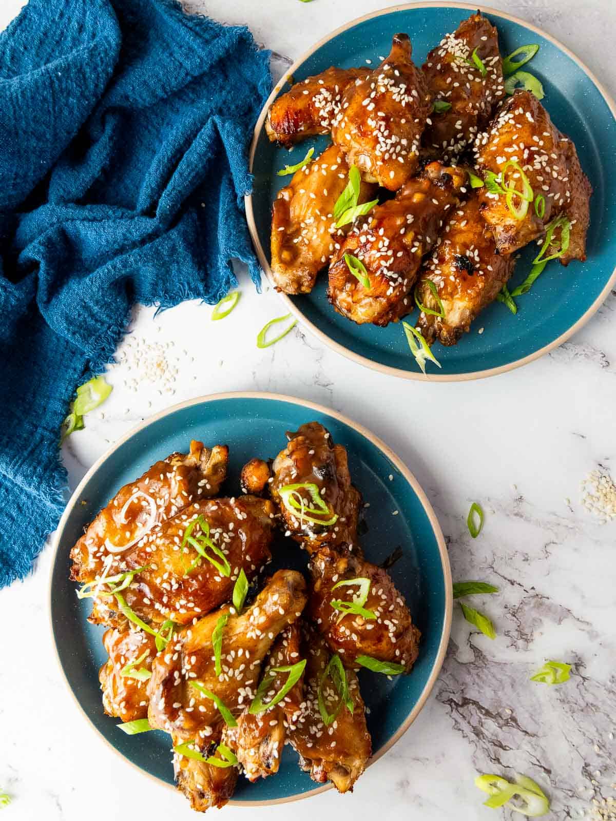 Two plates of Asian sticky chicken wings on a marble surface.