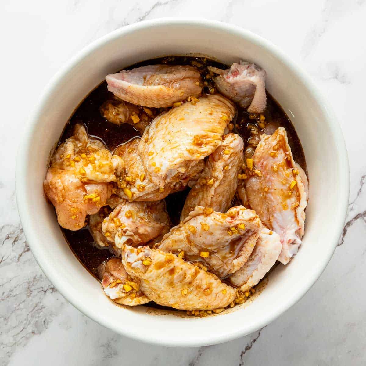 Marinated chicken wings in a white bowl.