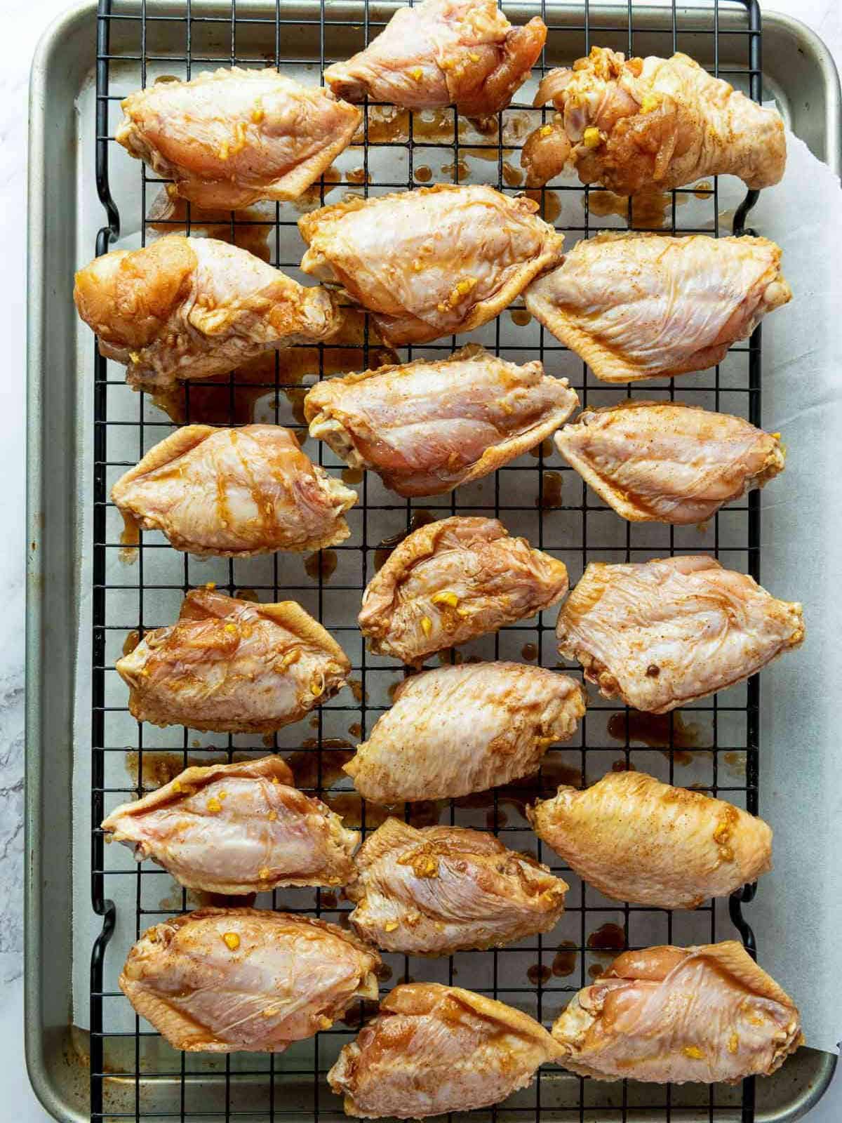 Marinated chicken wings placed on a wire rack over baking sheet.