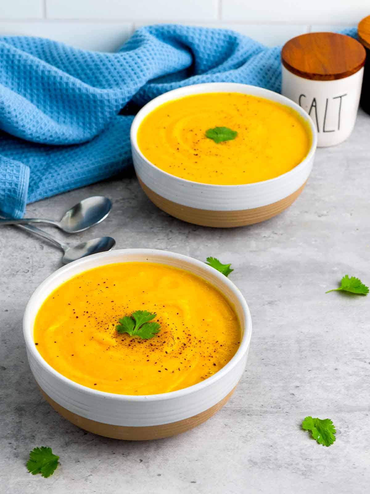 Two bowls of butternut squash soup on a grey surface.