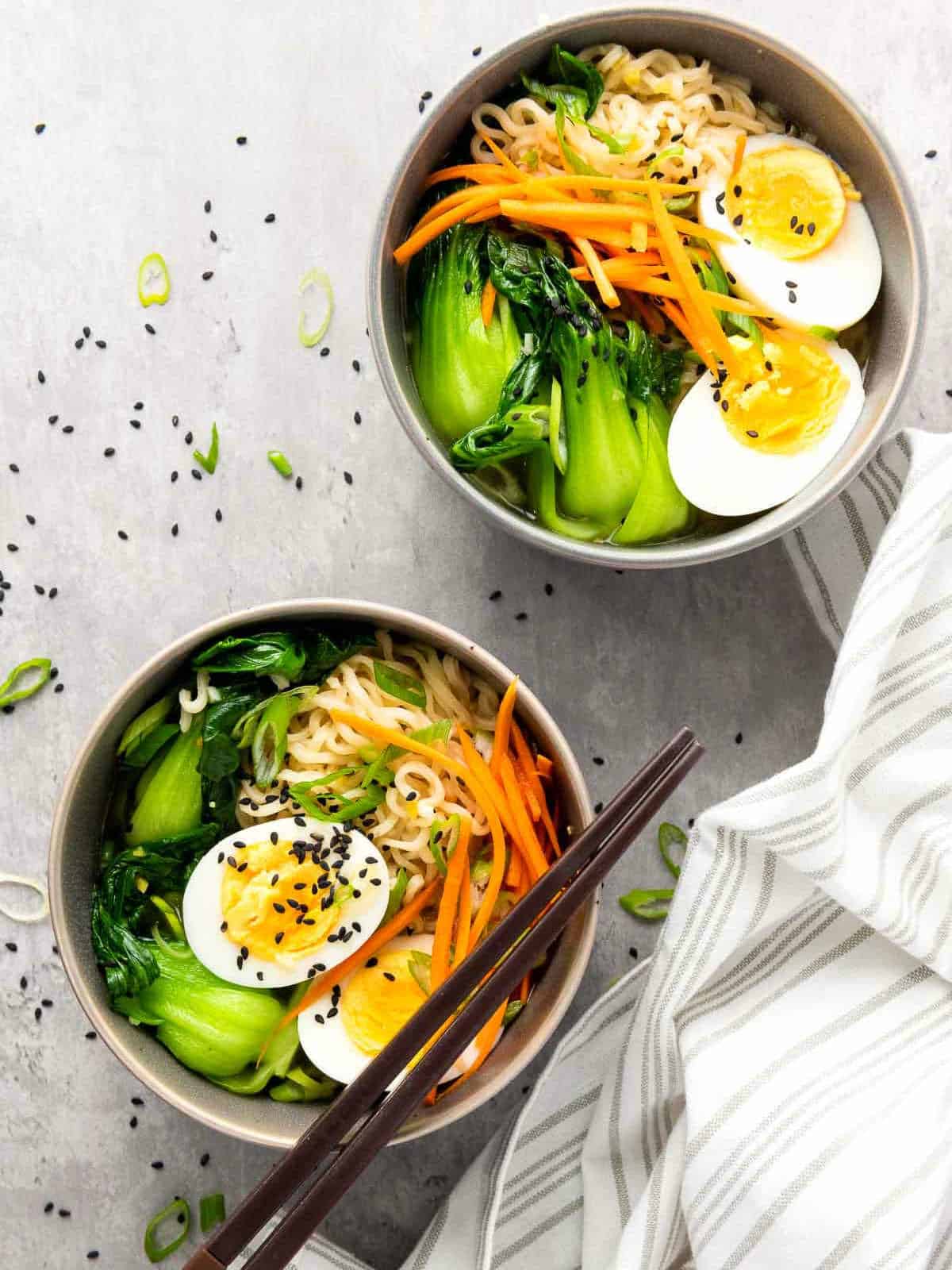 Two bowls of elevated ramen noodles placed on a grey surface.