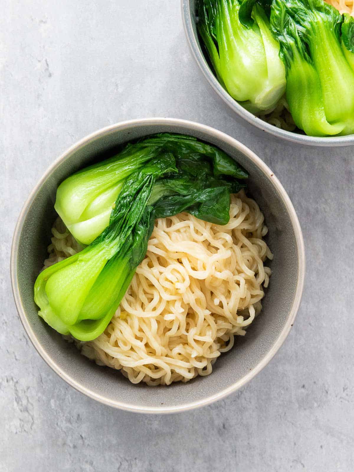 Assembling ramen bowls with noodles and bok choy.