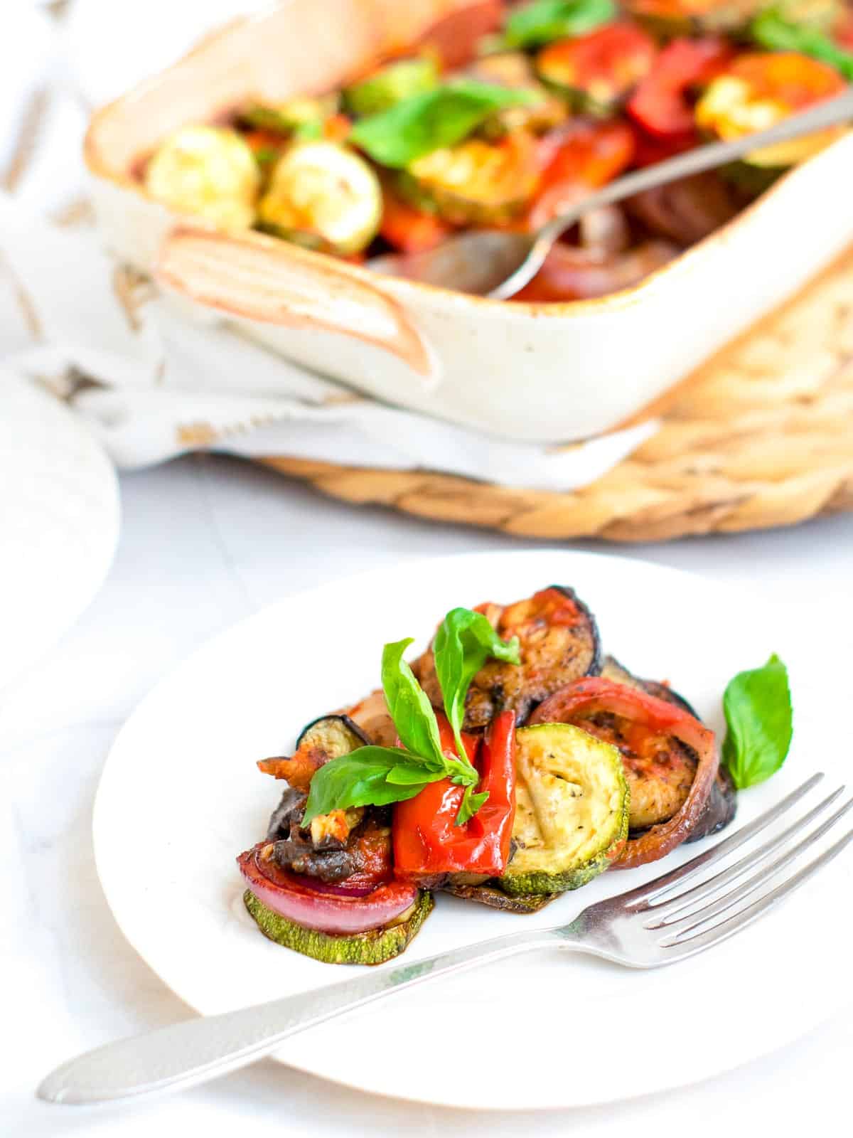 Side view of a plate of Ratatouille Casserole with casserole dish in the background.