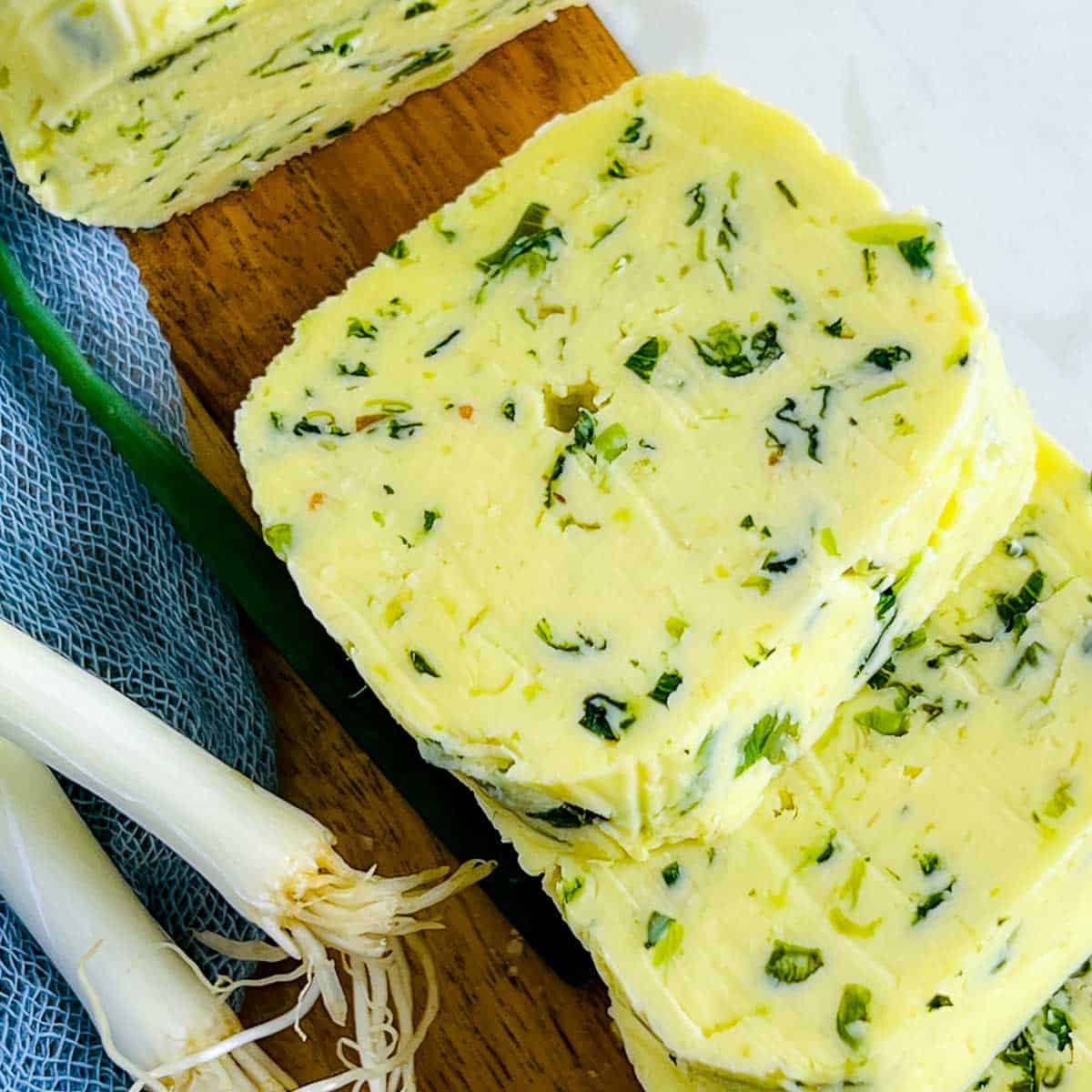 Slices of scallion butter on a wooden plate.