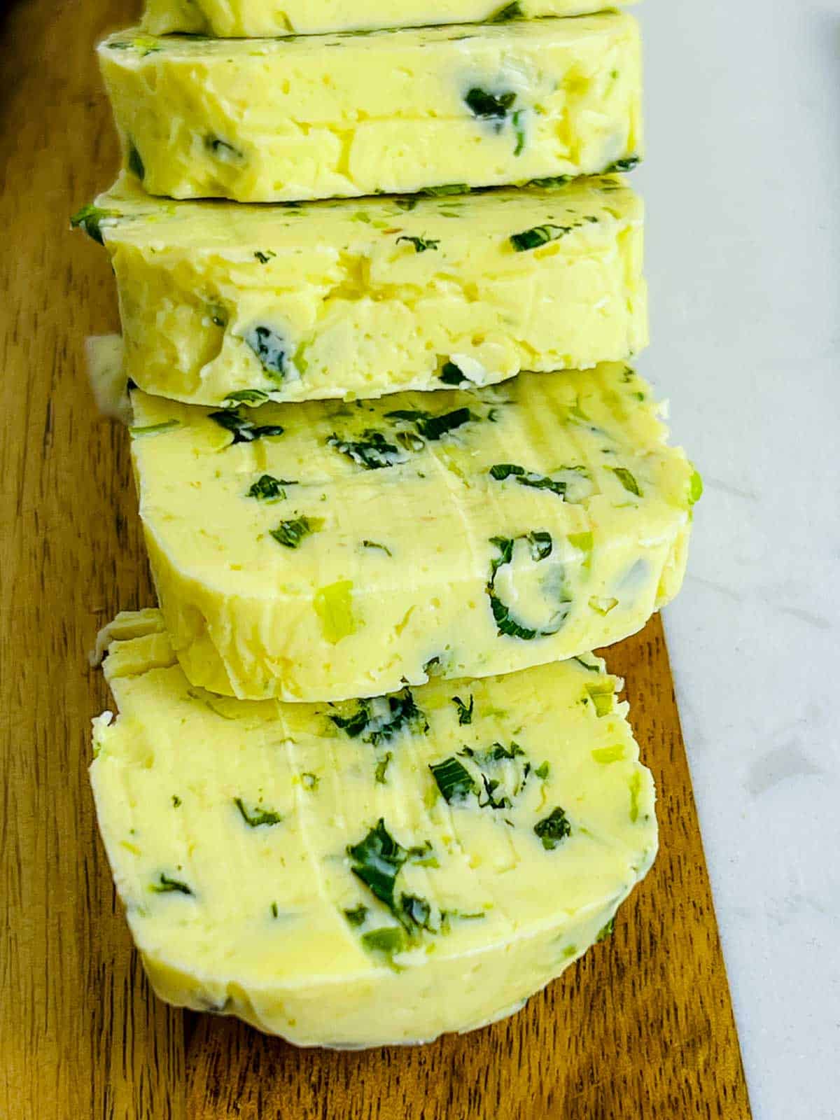 Close up of cut scallion butter on a wooden board.