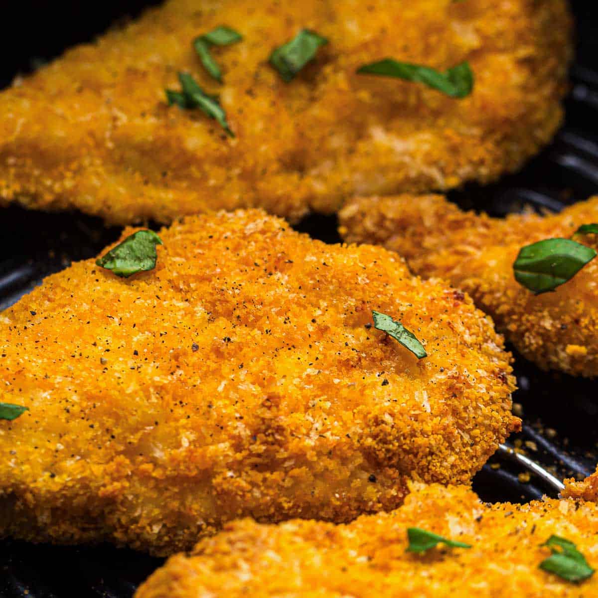 Close up of chicken cutlets placed in the air fryer basket.