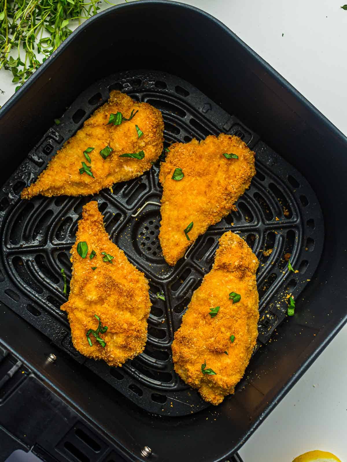 Chicken cutlet in air fryer basket garnished with parsley.